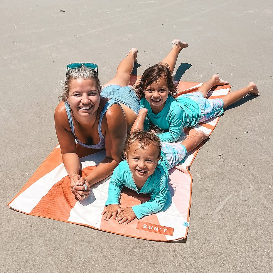 Two women and a child lying on a SUN'Y beach towel (Rays) at the beach