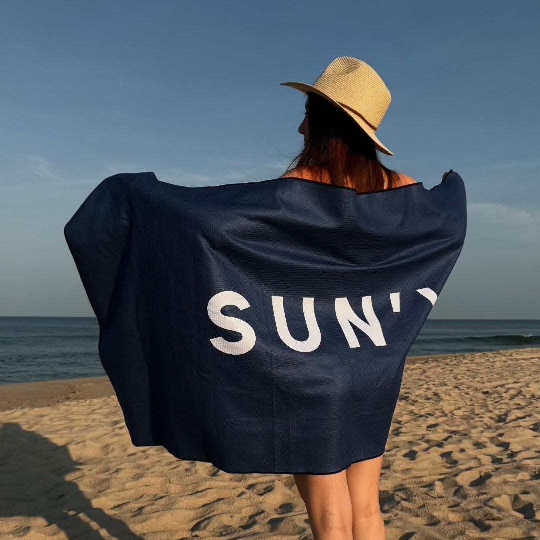 Person on a beach wearing a SUN'Y beach towel (Navy).